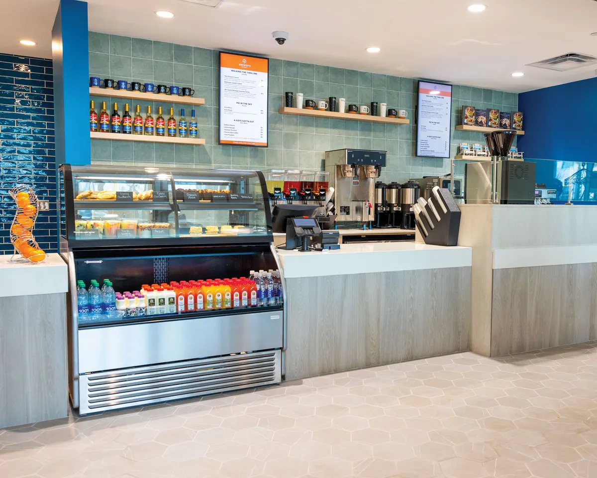 A cozy, well-lit interior featuring a display case filled with pastries, a beverage cooler, a coffee station, and a visible menu board. The seating area in the foreground invites guests to enjoy their drinks and snacks in comfort, creating a welcoming environment ideal for casual dining and relaxed gatherings.