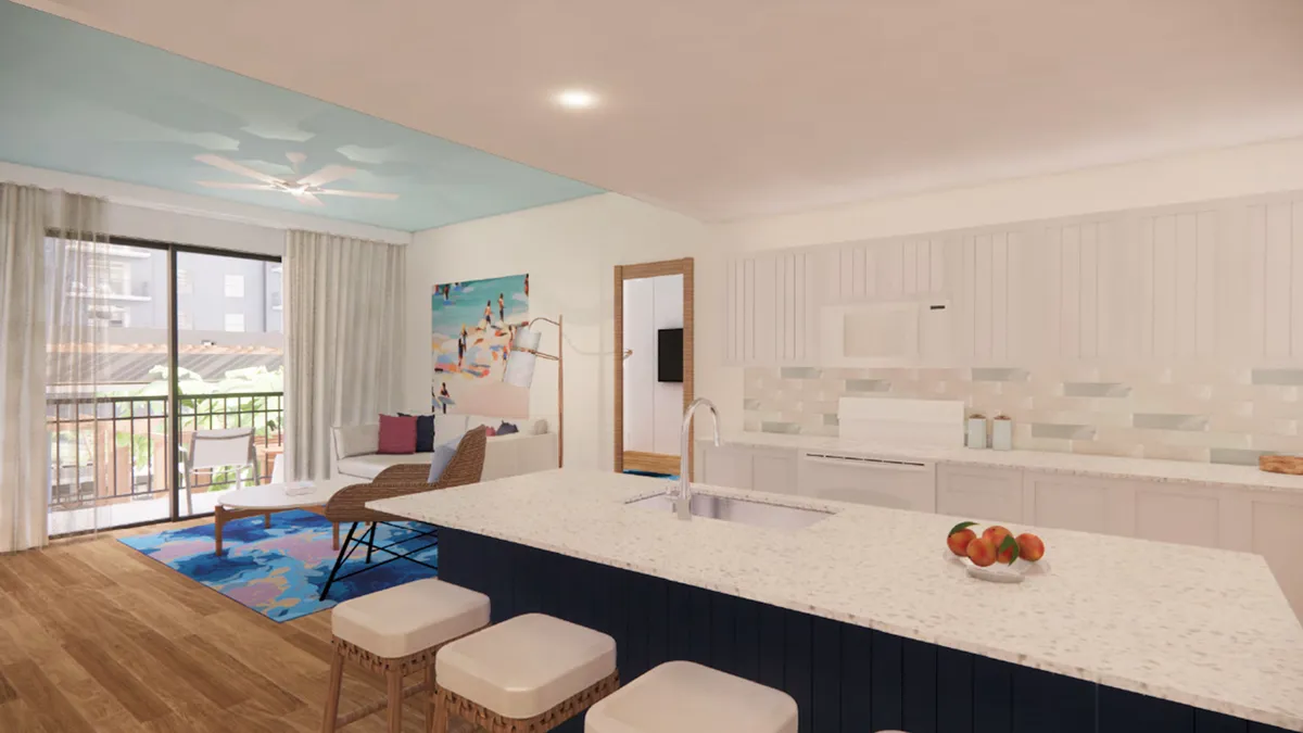 A luminous interior scene centering on a kitchen island, surrounded by colorful artwork and large windows that let in abundant daylight. The space feels open and cheerful—ideal for morning coffee or group activities, and closely resembles a living area adjacent to a balcony.