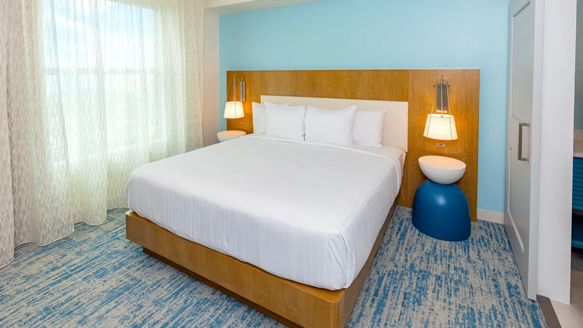 A tranquil king bedroom featuring a plush bed adorned with crisp white linens, soft bedside lamps casting a warm glow, and a decorative rug that adds a touch of style and comfort. The overall mood is restful and inviting, suggesting a serene sanctuary for parents or couples.